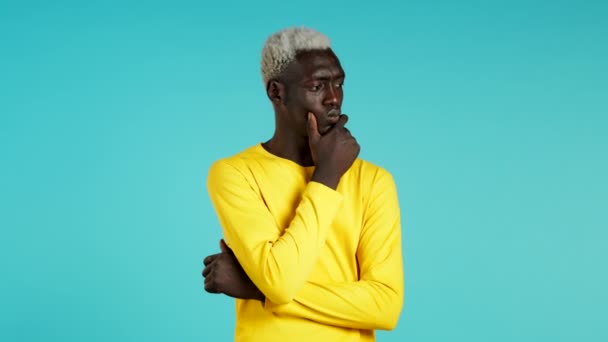 Πορτρέτο του νεαρού Αφροαμερικανού σκεπτόμενου άντρα που έχει την ιδέα να δείχνει με το δάχτυλο το μπλε φόντο του στούντιο. Χαμογελαστός χαρούμενος μαθητής που δείχνει ευφράδεια. — Αρχείο Βίντεο