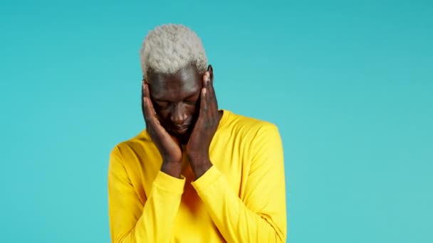 Jonge Afro-Amerikaanse man met hoofdpijn, studioportret. Man met handen op het hoofd, geïsoleerd op een blauwe achtergrond. Concept van problemen, geneeskunde, ziekte — Stockvideo
