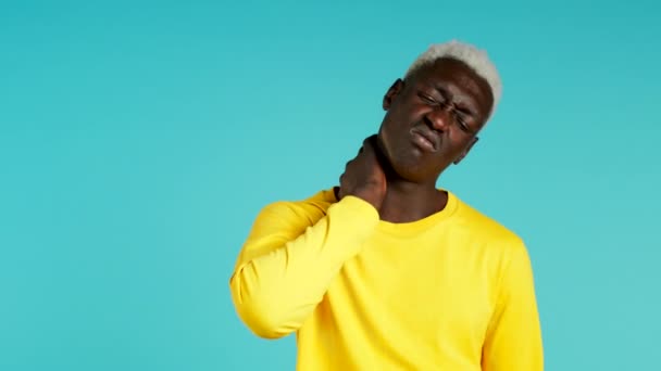 Joven afroamericano con dolor en el cuello, retrato de estudio. Tipo poniendo las manos en la garganta, aislado sobre fondo azul. Concepto de problemas, medicina, enfermedad — Vídeo de stock