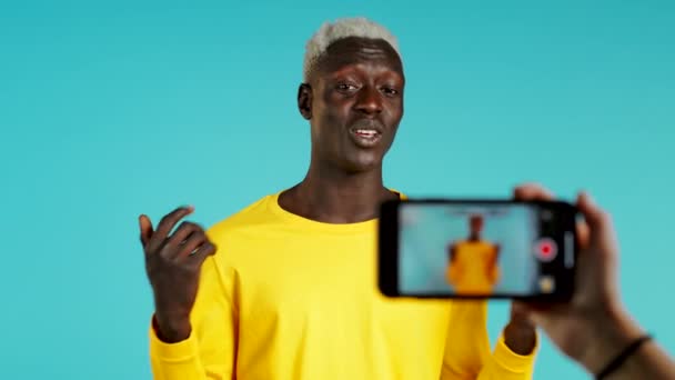 Lächelnder afrikanischer Blogger, der mit seinem Smartphone auf blauem Hintergrund ein neues Online-Videoblog namens vlog macht. Influencer spricht während Telefonkonferenz vor Kamera. — Stockvideo