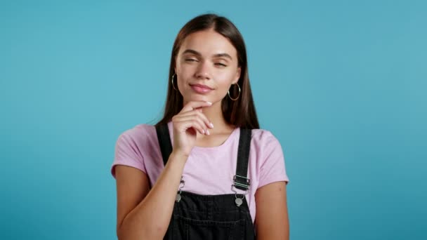 Sonriente chica feliz mostrando gesto eureka. Retrato de una joven pensando en una mujer que tiene un momento de idea apuntando con el dedo hacia arriba en el fondo azul del estudio. — Vídeo de stock