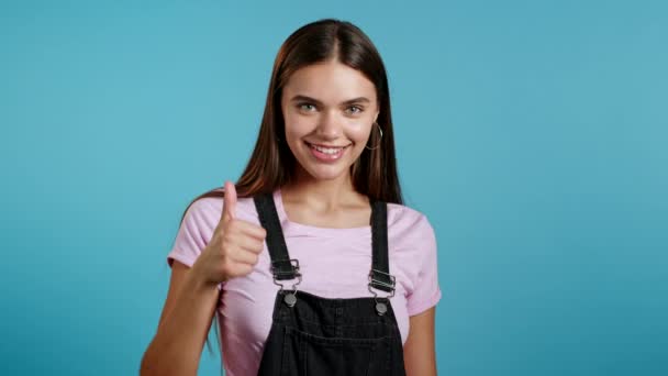 Mujer linda mostrando el pulgar hacia arriba signo sobre fondo azul. Chica joven y positiva sonríe a la cámara. Ganador. Éxito. Lenguaje corporal. — Vídeos de Stock