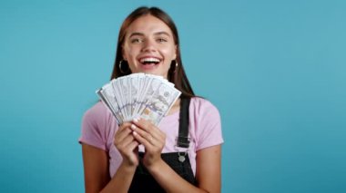 Şaşırtıcı derecede mutlu, heyecanlı bir kadın mavi duvarda Amerikan doları banknotları gösteriyor. Başarı, kazanç, zafer sembolü.