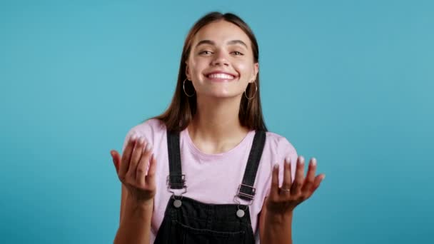 Hermosa mujer mostrando - Oye tú, ven aquí. Chica en general pedir unirse a ella, hace señas con abrazos de mano acogedor gesto. La señora se ve juguetona coqueta, invitando a venir. Fondo estudio azul. — Vídeos de Stock