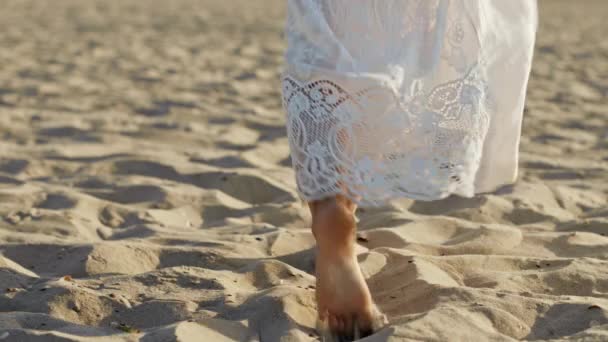 Πόδια του κοριτσιού φορώντας λευκό μακρύ φόρεμα με τα πόδια ξυπόλητη άμμο στη θάλασσα παραλία ή έρημο. Αργή κίνηση. Γυναίκα περπατά μακριά κάμερα — Αρχείο Βίντεο