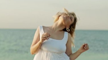 Beyaz elbiseli, sarı saçlı, deniz dibinde dans eden bir kadın. Kız müziğin ritmine göre hareket ediyor. Kadın eğleniyor. Gülümsüyor, saçları çok güzel titriyor. İnanılmaz pozitif görüntüler..