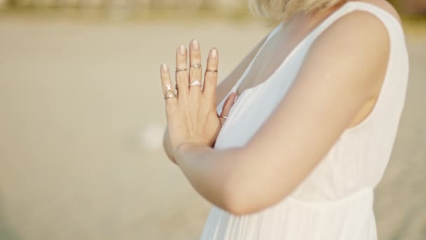 Mulher praticando ioga, namaste mudra gratidão sozinho na praia de areia na hora do pôr do sol verão. Menina de vestido branco. Religião, pureza, renúncia, conceito de espiritualidade. Movimento lento — Vídeo de Stock