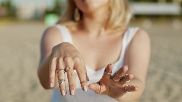 Hermosa mujer gitana joven demuestra con las manos la danza de la joyería boho. Chica en vestido blanco mostrando accesorios en la playa. En cámara lenta. Concepto de feminidad. — Vídeos de Stock