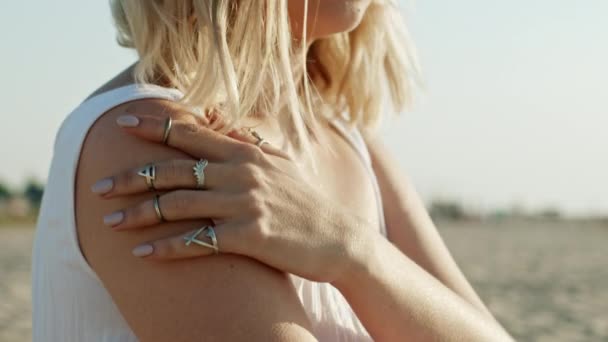 Young unrecognizable woman caressing her shoulder, strokes body on sandy beach. Beautiful girl touching her forearm. Hand with fashionable rings. Jewelry, fashion, healthy skin concept — Stock Video