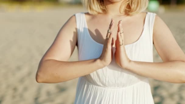 Nő jógázik, namaste hála mudra egyedül homokos strandon nyári naplementekor. Fehér ruhás lány. Vallás, tisztaság, lemondás, spirituális felfogás. Lassú mozgás. — Stock videók