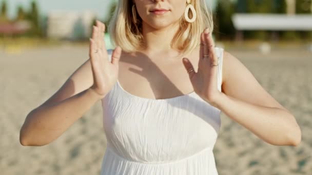 Vrouw die yoga beoefent, namaste dankbaarheid Mudra alleen op zandstrand bij zonsondergang in de zomer. Meisje in witte jurk. Religie, zuiverheid, berusting, spiritualiteit concept. Langzame beweging — Stockvideo