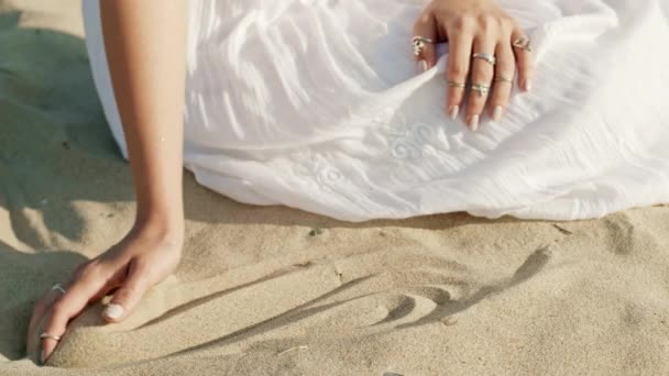 Frauenhände spielen am Strand mit Sand. Schöne Szene von jungen Boho Zigeunermädchen in weißem Kleid mit Ringen, die Körner berühren. Zeitlupe — Stockvideo