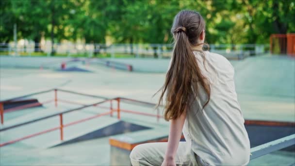 Jovem adolescente com cabelos longos sentada sozinha no parque de skate. Mulher irreconhecível à espera de amigos. — Vídeo de Stock