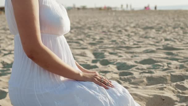 Nierozpoznawalna kobieta w białej sukience i boho pierścienie na ramionach siedzi sama na piaszczystej plaży. Medytacja, zanurzenie w świecie wewnętrznym, jedność z naturą. — Wideo stockowe