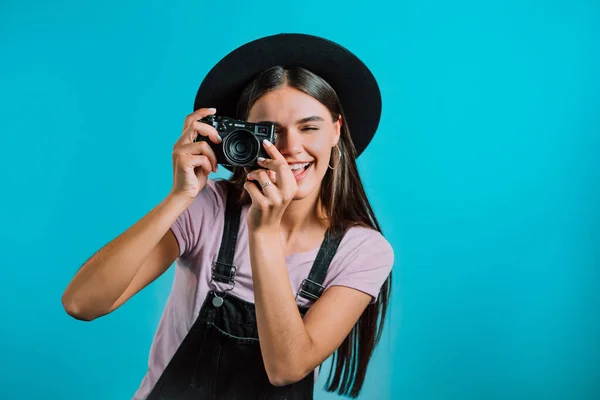 Mladá hezká žena v celkovém pořizuje snímky s DSLR kamerou nad modrým pozadím ve studiu. Dívka se usmívá a baví jako fotograf. — Stock fotografie