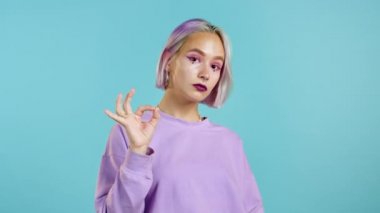 Renkli saçlı hoş bir kadın mavi arka planda iyi işareti gösteriyor. Olumlu genç kız iyi. Kazandım. Başarı. Vücut dili. 