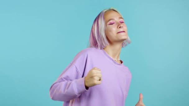 Ragazza hipster con tinti viola acconciatura ballare energicamente e divertente su sfondo blu studio. Bella ragazza in viola. Festa, felicità, libertà, concetto di gioventù. — Video Stock