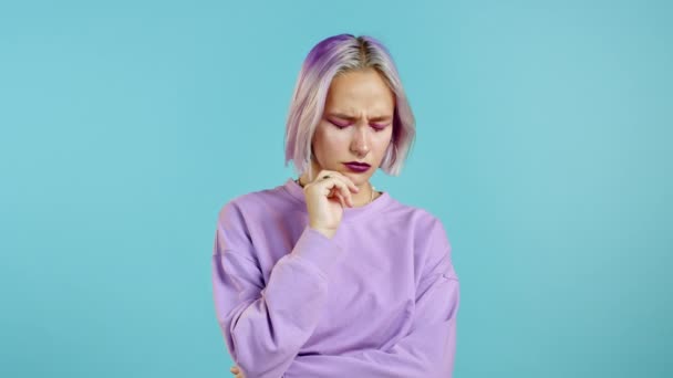 Muchacha seria con pelo violeta mostrando gesto eureka. Retrato de una joven pensando en una mujer que tiene un momento de idea apuntando con el dedo hacia arriba en el fondo azul del estudio. — Vídeos de Stock