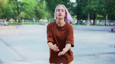Genç dansçı kız hip-hop hareketlerinden hoşlanıyor. Menekşe boyalı saçlı modern kadın yaz aylarında kaykay parkında serbest dans gösterisi yapıyor. Yavaş çekim.