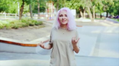 Genç dansçı kız hip-hop hareketlerinden hoşlanıyor. Pembe boyalı saçlı modern kadın yaz aylarında kaykay parkında serbest dans gösterisi yapıyor. Yavaş çekim.