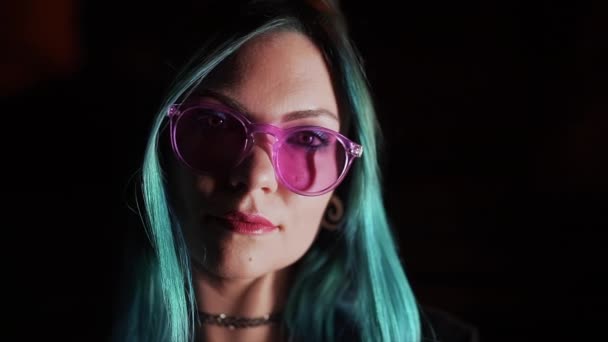 Retrato de una chica bonita enigmática milenaria con un inusual peinado azul teñido por la noche. Misteriosa mujer hipster en gafas. — Vídeo de stock