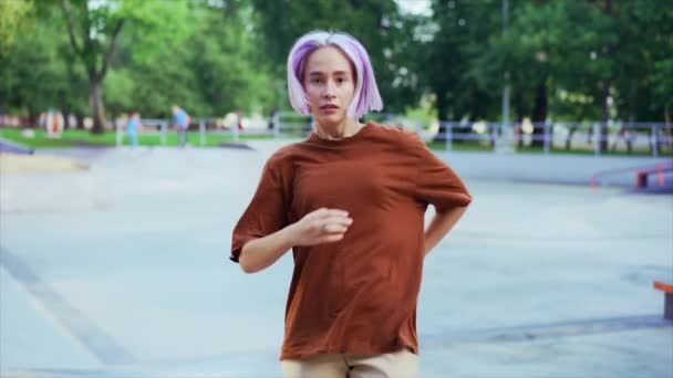 Genç dansçı kız hip-hop hareketlerinden hoşlanıyor. Menekşe boyalı saçlı modern kadın yaz aylarında kaykay parkında serbest dans gösterisi yapıyor. Yavaş çekim. — Stok video
