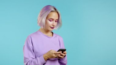 Hippi kadın mesajlaşıyor, akıllı telefondaki uygulamayı kullanıyor. İnternet 'te cep telefonuyla renkli saç sörfü yapan güzel bir kız. Mavi stüdyo portresi.