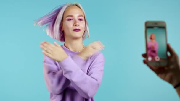 Lächelnde Vlogger-Hipsterfrau, die ein Video von sich aufnimmt, wie sie vor der Smartphone-Kamera auf blauem Hintergrund tanzt. Influencer macht lustigen Social-Media-Clip — Stockvideo