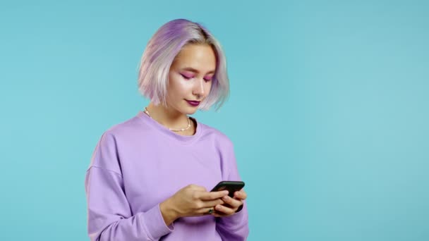 Хіпстерська жінка смс-повідомлення, використовуючи додаток на смартфоні. Красива дівчина з барвистим волоссям, що серфінгує Інтернет з мобільним телефоном. Блакитний студійний портрет . — стокове відео