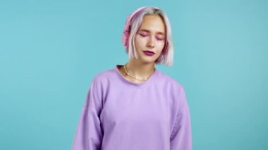 Mor saçlı güzel bir kız müzik dinliyor, gülümsüyor, kulaklıkla kulaklıkla dans ediyor mavi arka planda. Müzik, dans, radyo konsepti, yavaş çekim.