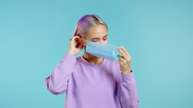 Genç ve güzel bir kız koronavirüs salgını sırasında yüz maskesi takıyor. Mavi arka planda bir portre. COVID-19 salgınına karşı solunum cihazıyla koruma