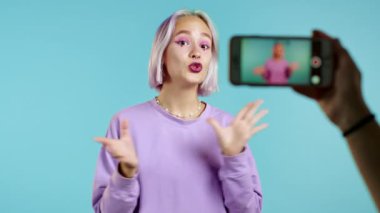 Gülümseyen moda blogcusu hipster kadın mavi arka planda akıllı telefonuyla çevrimiçi yeni video blogu, vlog yapıyor. Konferans kayıtları sırasında kameraya konuşan nüfuzlu kişi.