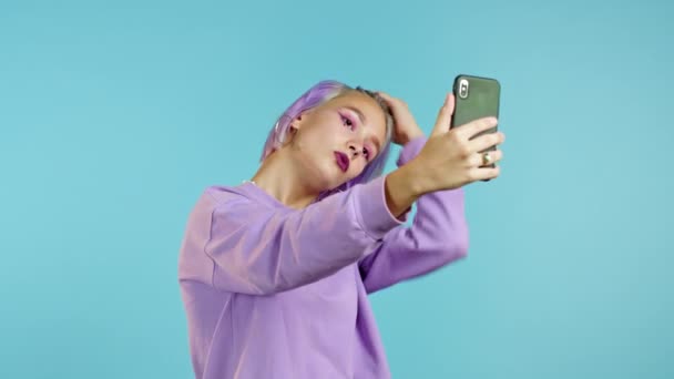 Ragazza alla moda manierato facendo selfie su smartphone su sfondo blu. Donna con acconciatura viola tinta. Tecnologia, dispositivo mobile, concetto di social network — Video Stock