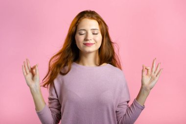 Sakin bir kadın dinleniyor, meditasyon yapıyor. Kız sakinleşiyor, pembe stüdyo arka planında derin derin nefes alıyor.