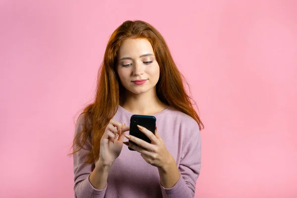 Woman sms texting, using app on smartphone. Pretty girl surfing internet with mobile phone. Pink studio portrait.