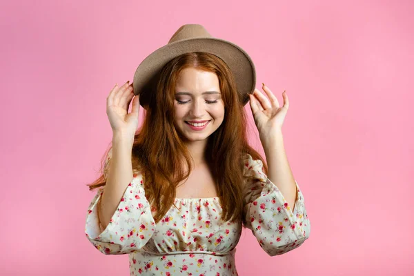 Giovane donna sorridente con acconciatura rossa e cappello. Ritratto di bella ragazza carina su sfondo rosa studio parete. — Foto Stock