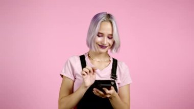 Hippi kadın mesajlaşıyor, akıllı telefondaki uygulamayı kullanıyor. İnternet 'te cep telefonuyla renkli saç sörfü yapan güzel bir kız. Pembe stüdyo portresi.