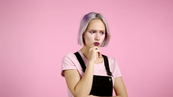 Pensar en una chica seria con el pelo violeta cuenta en mente. Retrato de una joven mujer pensante mirando hacia arriba y alrededor sobre fondo rosa. — Vídeos de Stock