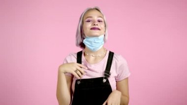 Memnun kadın koruyucu maskeyi çıkardı ve salgın hastalığın sembolü olarak yere attı. Pembe stüdyo arka planı.