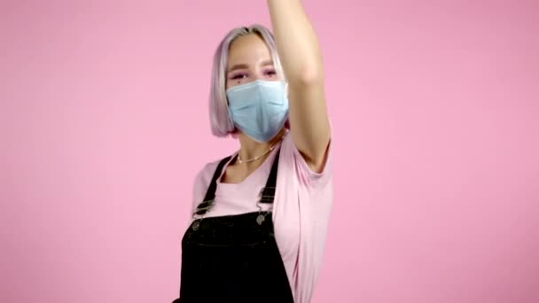 Mooie hipster vrouw in beschermende masker dansen met kleurrijke kapsel energiek en actief op roze studio achtergrond. Schattig meisjes portret. Feest, geluk, vrijheid, jeugdconcept. — Stockvideo