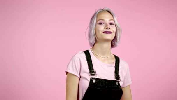 Belle femme hipster avec des cheveux violets colorés souriant, flirtant à la caméra sur fond de mur rose. mignon tendance ludique filles portrait — Video