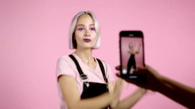 Gülümseyen vlogger hipster kadın pembe arka planda kendini akıllı telefon kamerasının önünde dans ederken videoya kaydediyor. Nüfuz Edici komik sosyal medya klibi yapıyor