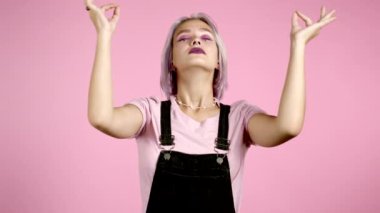 Sakin, mor saçlı, meditasyon yapan hippi kadın. Kız sakinleşiyor, pembe stüdyo arka planında derin derin nefes alıyor.