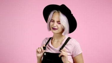 Şapkalı güzel hippi kadın ve pembe stüdyo arka planında dans eden menekşe rengi saç stili. Şirin kızlar portresi. Parti, mutluluk, özgürlük, gençlik kavramı.