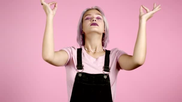 Mujer hipster calma con el pelo violeta relajante, meditando. Chica se calma, respira profundamente con mudra om sobre fondo de estudio rosa — Vídeos de Stock