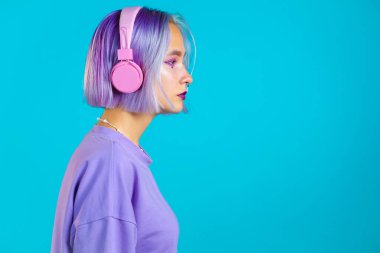 Mor saçlı güzel bir kız müzik dinliyor, gülümsüyor, kulaklıkla kulaklıkla dans ediyor mavi arka planda. Müzik, dans, radyo konsepti