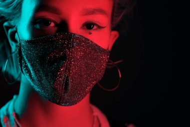 Gece kulübünde sahte elmaslarla dans eden koruyucu maskeli, güzel, modaya uygun genç bir kadın. Neon renkli ışık. Moda modelinin yakın plan portresi.