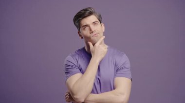 Düşünen adam Violet 'in arka planına bakıyor. Eflatun tişörtlü dalgın adam, yüz ifadeleri. Yakışıklı erkek manken cevabı. Yüksek kalite 4k