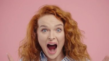 Şaşırtıcı derecede çekici kızıl kıvırcık kadın, vay canına diyor, inanamıyorum. İlgi çekmeye çalışan etkileyici bir bayan. Satış kavramı, karlı bir teklif. Pembe arka planda heyecanlı bir öğrenci kız. Yüksek kalite 4k