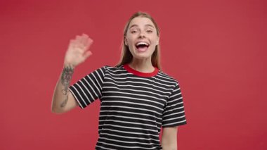 Dost canlısı genç Amerikalı kadın el sallıyor - merhaba, selam, kaos, adios. Ayrılıyorum, kameraya hoşça kal de. Kırmızı stüdyo arka planındaki güzel bayan. Yüksek kalite 4k